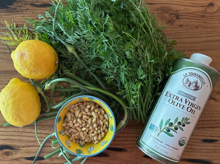 Carrot tops, lemons, pine nuts and olive oil displated on a table