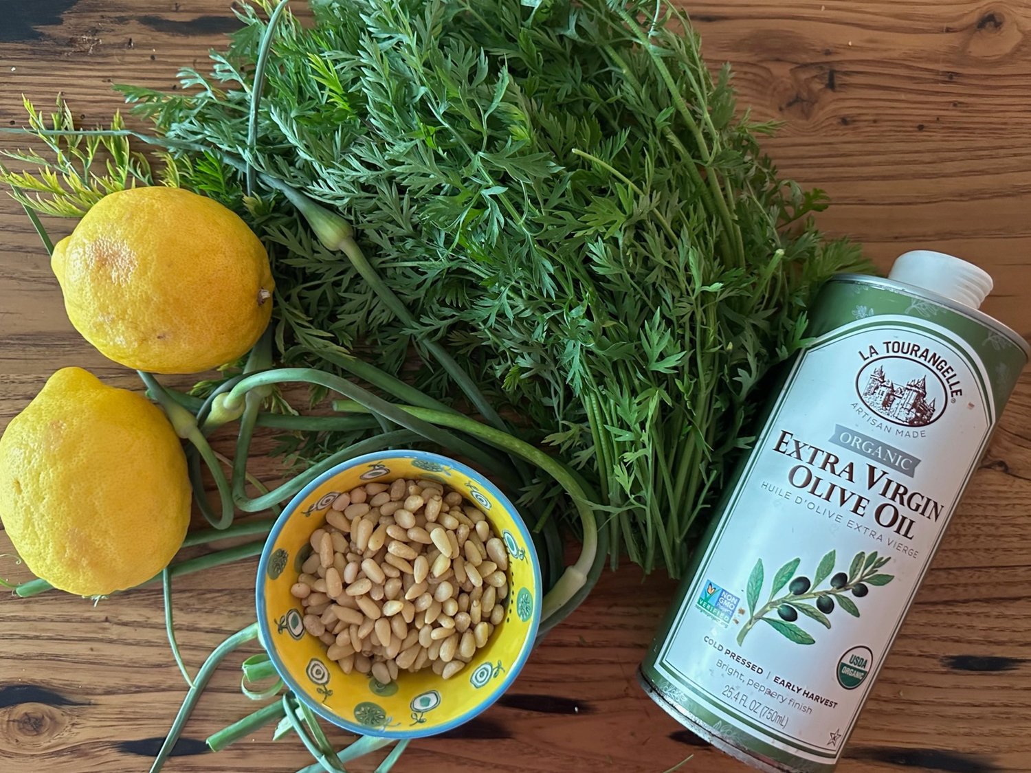 Carrot tops, lemons, pine nuts and olive oil displated on a table